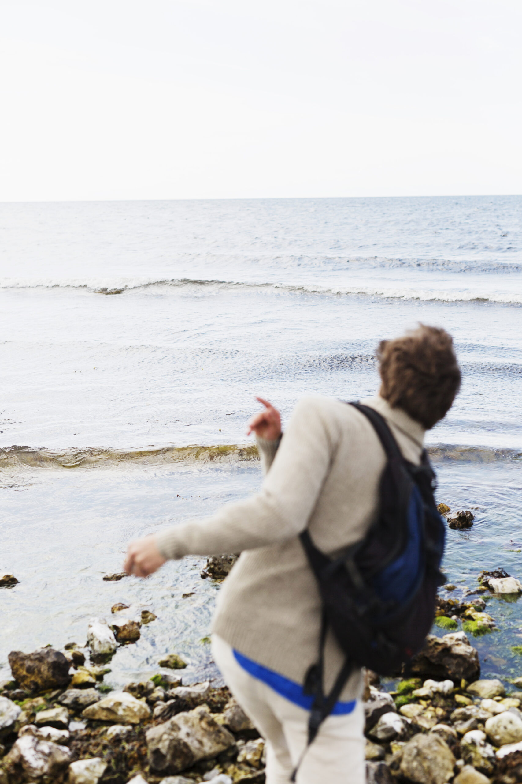 Rear view of man throwing stones in water at beach