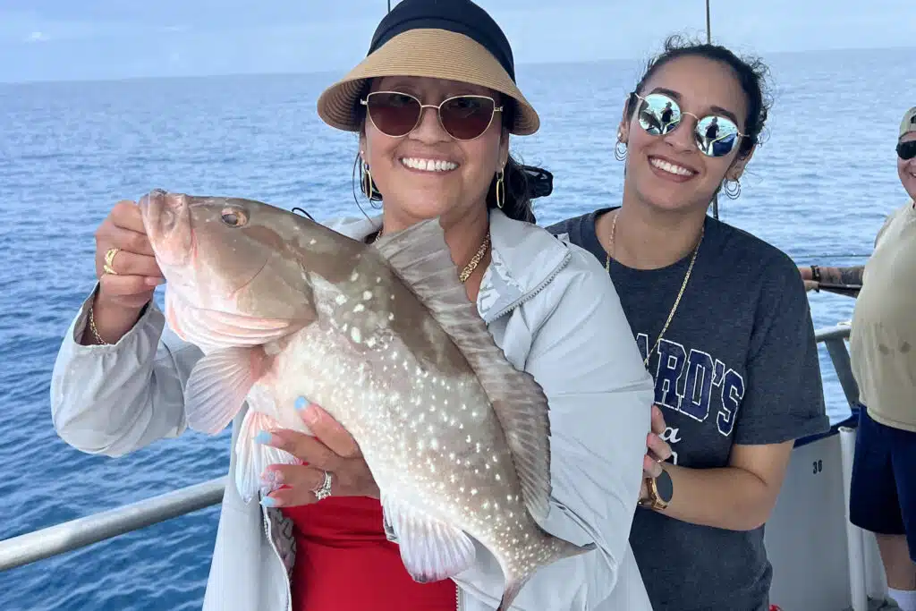 ladies holding a beautiful red grouper onboard hubbards marina nearshore trip